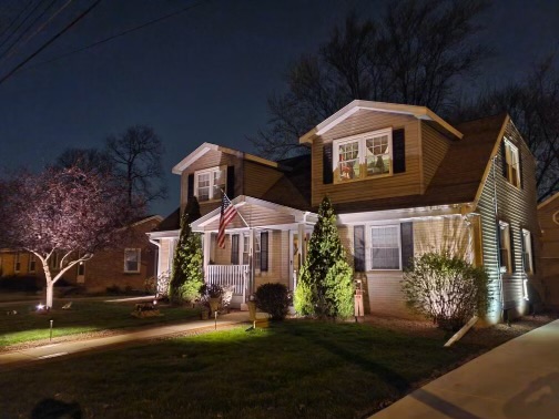 Under the night sky, a picturesque house nestled amidst a well-kept lawn and adorned with beautiful trees, creating a serene and enchanting ambiance.