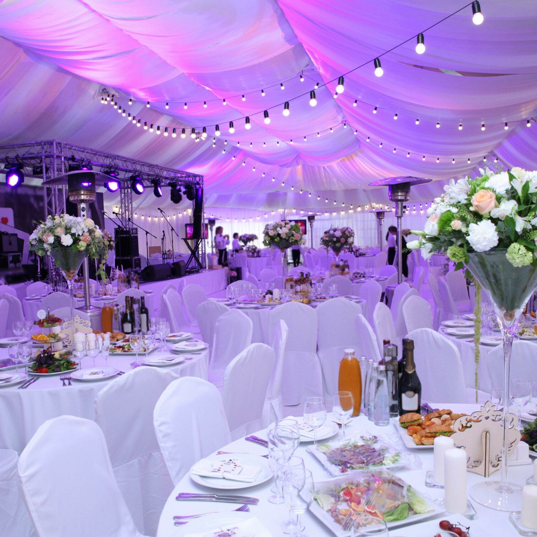 In the outdoor wedding tent, the wedding hall awaits the arrival of guests, featuring white chairs and elegant decor, setting the stage for a perfect and memorable celebration.